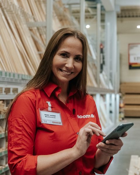 Mitarbeiterin im toom-Markt nutzt Smartphone; Mitarbeiter App, Employee Experience Platform sichtbar.