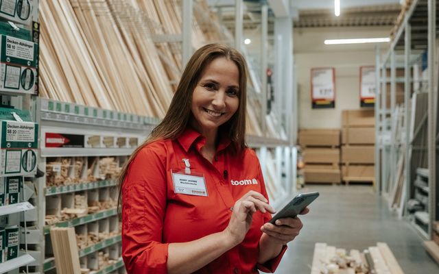 Mitarbeiterin im toom-Markt nutzt Smartphone; Mitarbeiter App, Employee Experience Platform sichtbar.