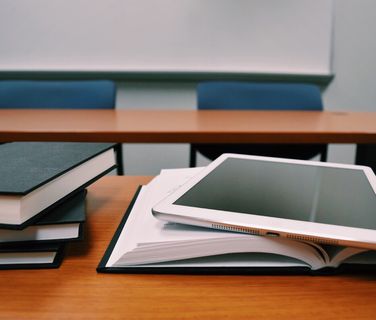 Tablet und BĂĽcher auf einem Tisch in einem leeren Klassenraum, Fokus auf digitale Lernumgebung.