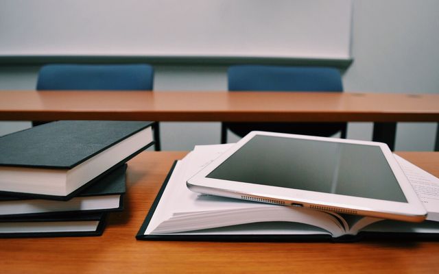 Tablet und Bücher auf einem Tisch in einem leeren Klassenraum, Fokus auf digitale Lernumgebung.