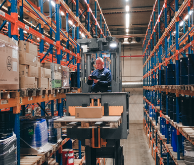 Warehouse worker uses digital device among shelves, highlighting frontline empowerment and Ops.