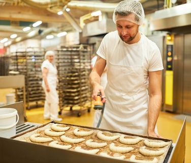 Baker in white uniform preparing croissants in a commercial bakery; industrial kitchen setting.
