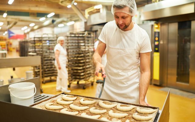 Baker in white uniform preparing croissants in a commercial bakery; industrial kitchen setting.