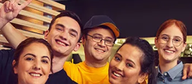 Five McDonalds workers in uniform smiling and posing together inside a restaurant.