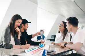 Diverse team collaborating and laughing at a table, showing authentic teamwork and creativity.
