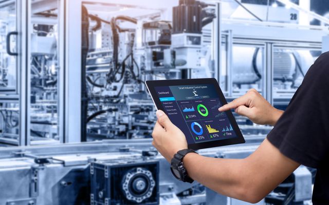 Person uses tablet with Smart Industrial Control System dashboard to boost manufacturing productivity.