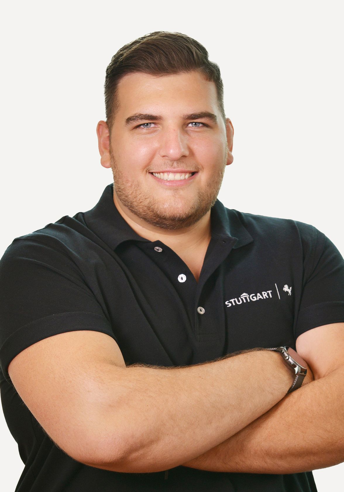 Smiling man in black STUTTGART polo shirt, arms crossed, neutral background.