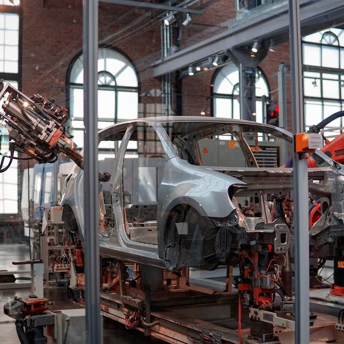 Robotic arms assembling a car frame in a factory setting.