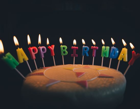 Runde Fondant-Torte mit brennenden HAPPY BIRTHDAY-Kerzen in bunten Buchstaben.