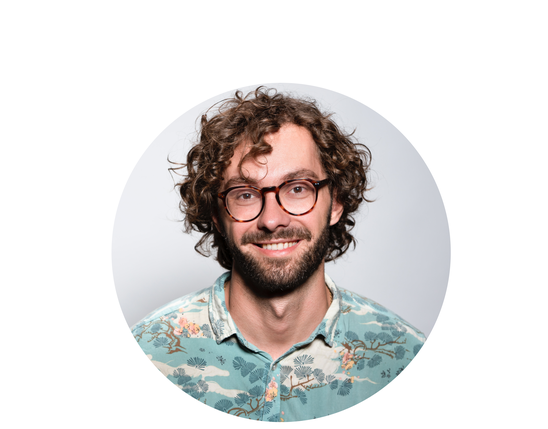 Portrait of a smiling man with curly hair and glasses, wearing a floral shirt on white background.