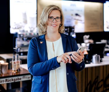 Businesswoman in McCafé using smartphone, smiling; no visible B2B-SaaS UI or keywords present.