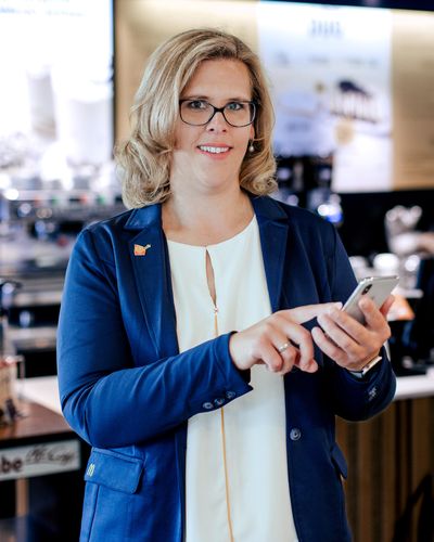 Businesswoman in McCafé using smartphone, smiling; no visible B2B-SaaS UI or keywords present.