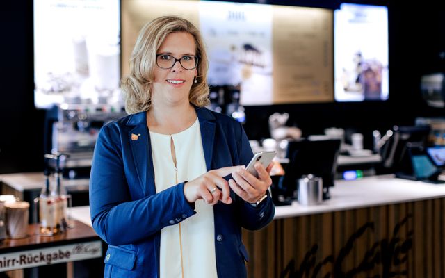 Businesswoman in McCafé using smartphone, smiling; no visible B2B-SaaS UI or keywords present.