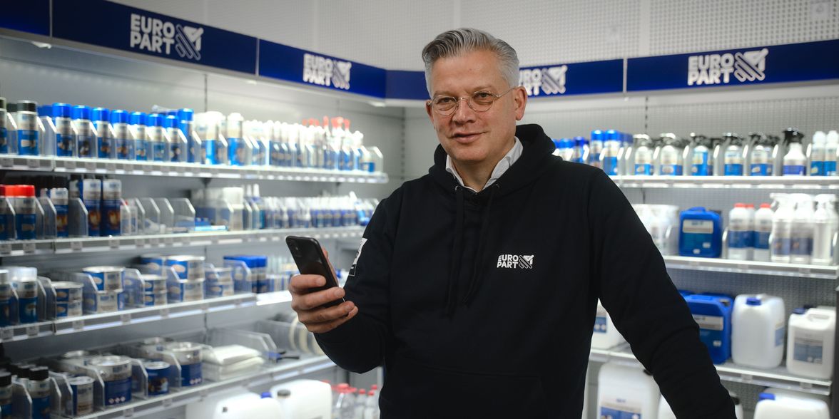 Man in EURO PART hoodie holding smartphone in store aisle with shelves of automotive products.