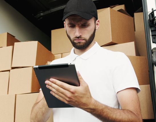 Delivery worker uses tablet in front of stacked boxes, optimizing logistics with Mitarbeiter App.