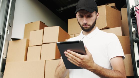 Delivery worker uses tablet in front of stacked boxes, optimizing logistics with Mitarbeiter App.