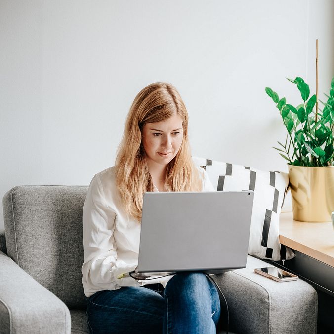 Woman working remotely on a laptop in a home office with a plant and coffee mug nearby.