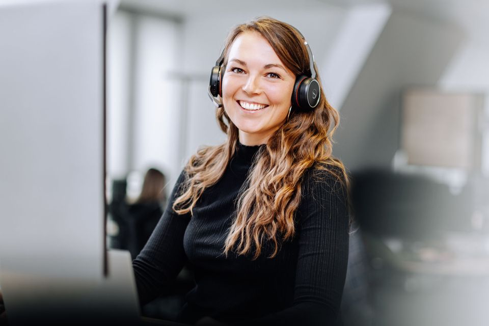 Smiling woman with headset at desk, modern office, employee engagement, marketing, HR-Software.