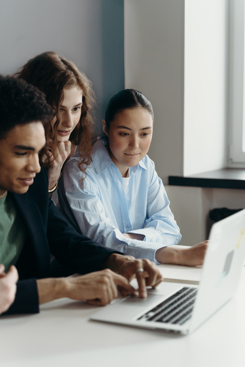 Three people collaborate at a laptop, no visible UI; environment is a modern office.