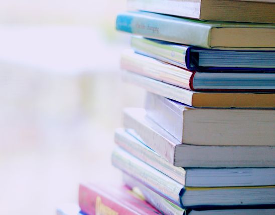 Stack of colorful books on a table, focus on spines, blurred background, no visible text.