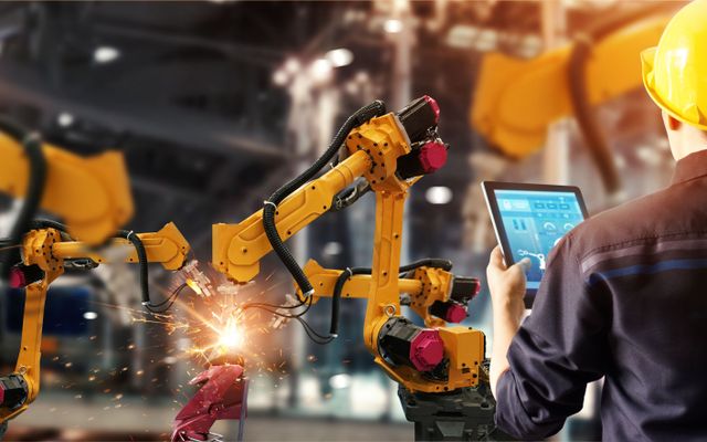 Worker steuert Roboterarme mit Tablet; digital workplace, Manufacturing, Employee Experience Platform.