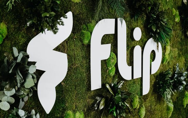 Large Flip logo on a green, plant-covered wall; decorative branding display.