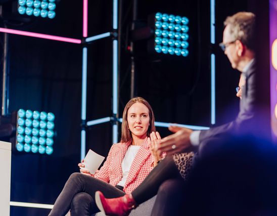 Panel discussion at digital conference, neon lights, two people talking, modern tech event atmosphere.