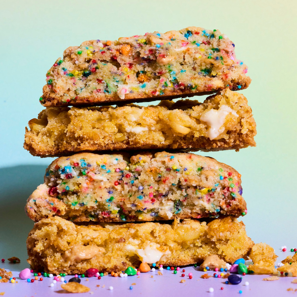 Stack of colorful cookies with sprinkles and marshmallow pieces against a pastel gradient background, surrounded by sprinkles.