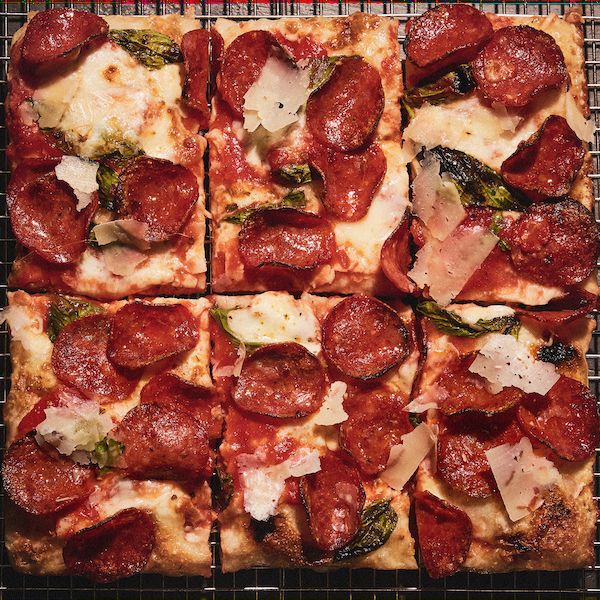 Square pizza with pepperoni, cheese, and basil on a wire rack, cut into six slices.
