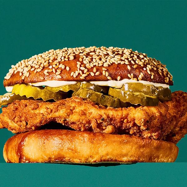 A crispy chicken sandwich with pickles and sauce, served on a sesame seed bun against a solid green background.