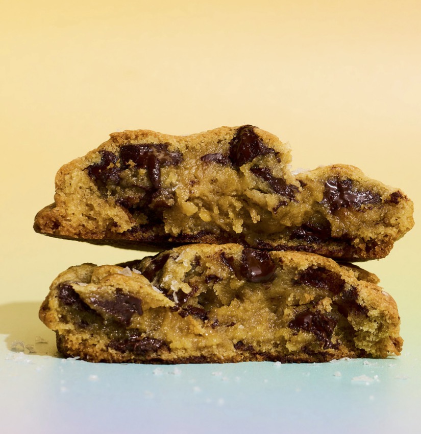 Two halves of a chocolate chip cookie stacked, revealing a gooey, chocolate-filled center against a pastel gradient background.