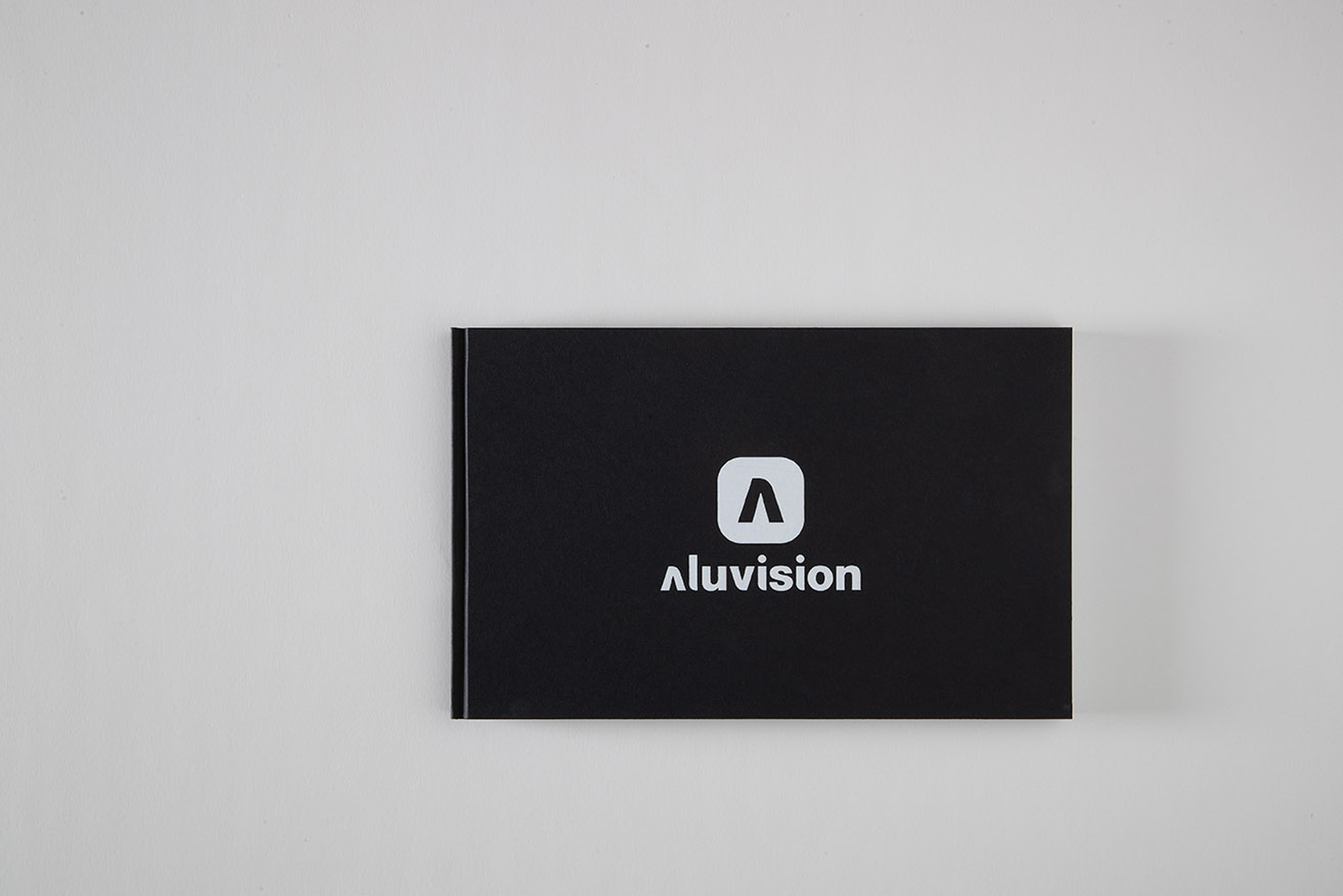 A black rectangular booklet with the Aluvision logo and name in white, placed on a light background.