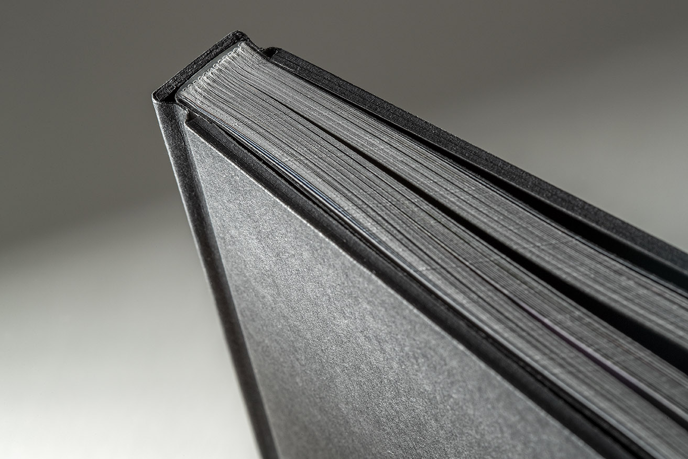 Close-up of a black hardcover book with visible pages and a textured binding, shot at an angle.