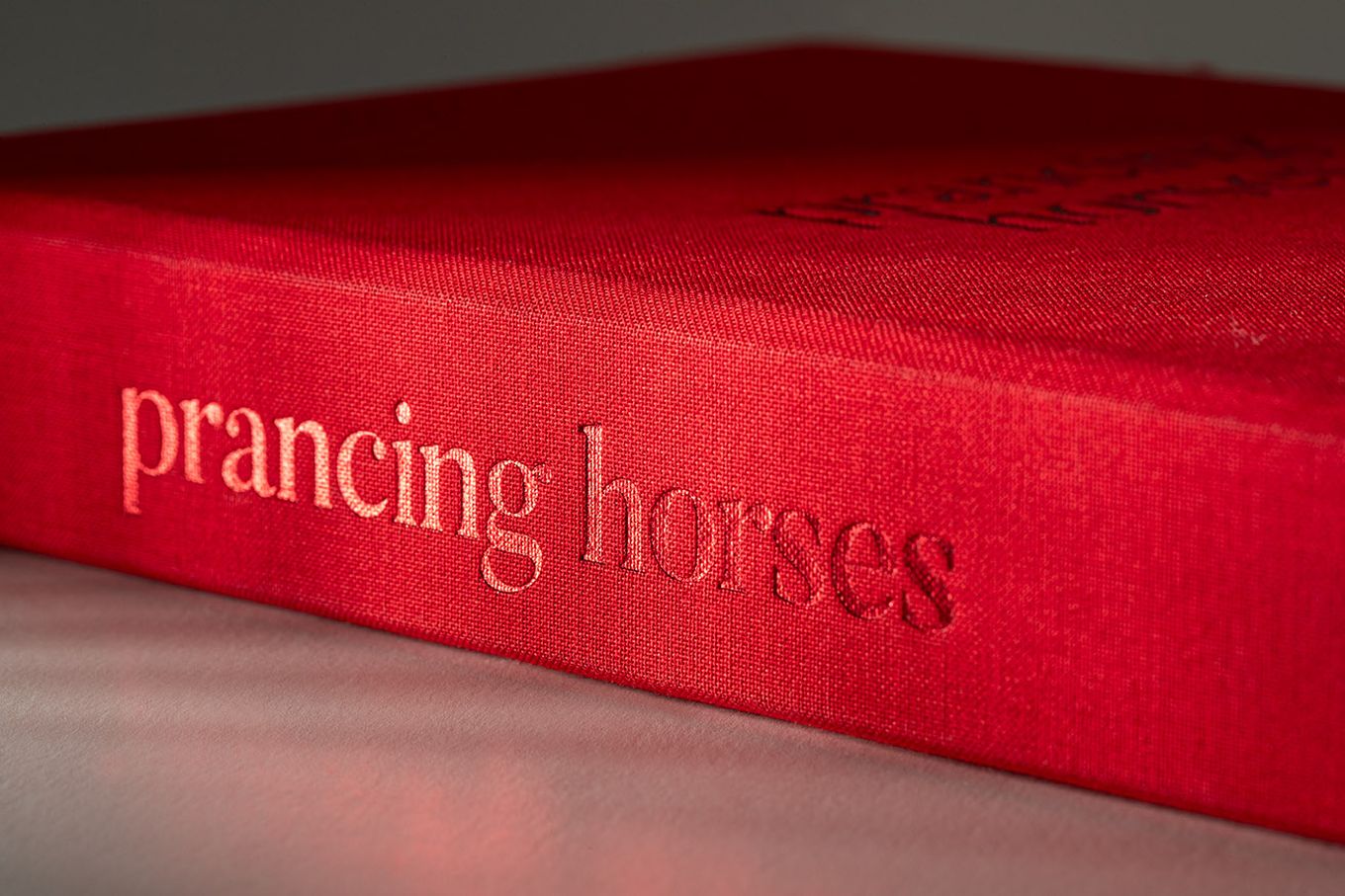 A red book titled "prancing horses" lies on a light gray surface.