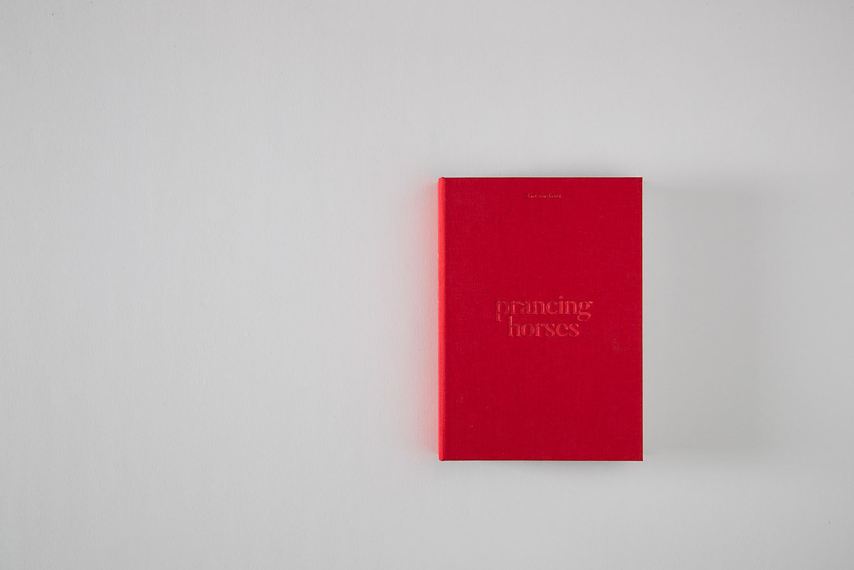 A red book titled "prancing horses" lies on a light gray surface.