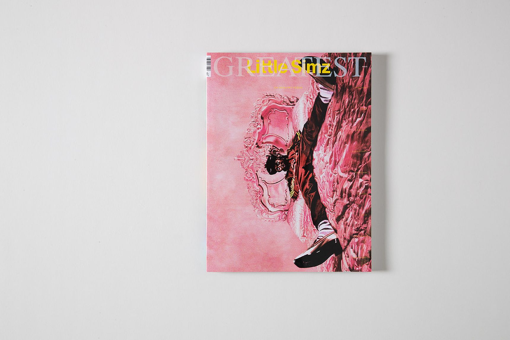 A magazine cover with a pinkish background featuring a man lying on a bed with ornate headboard, wearing casual clothing and sneakers.
