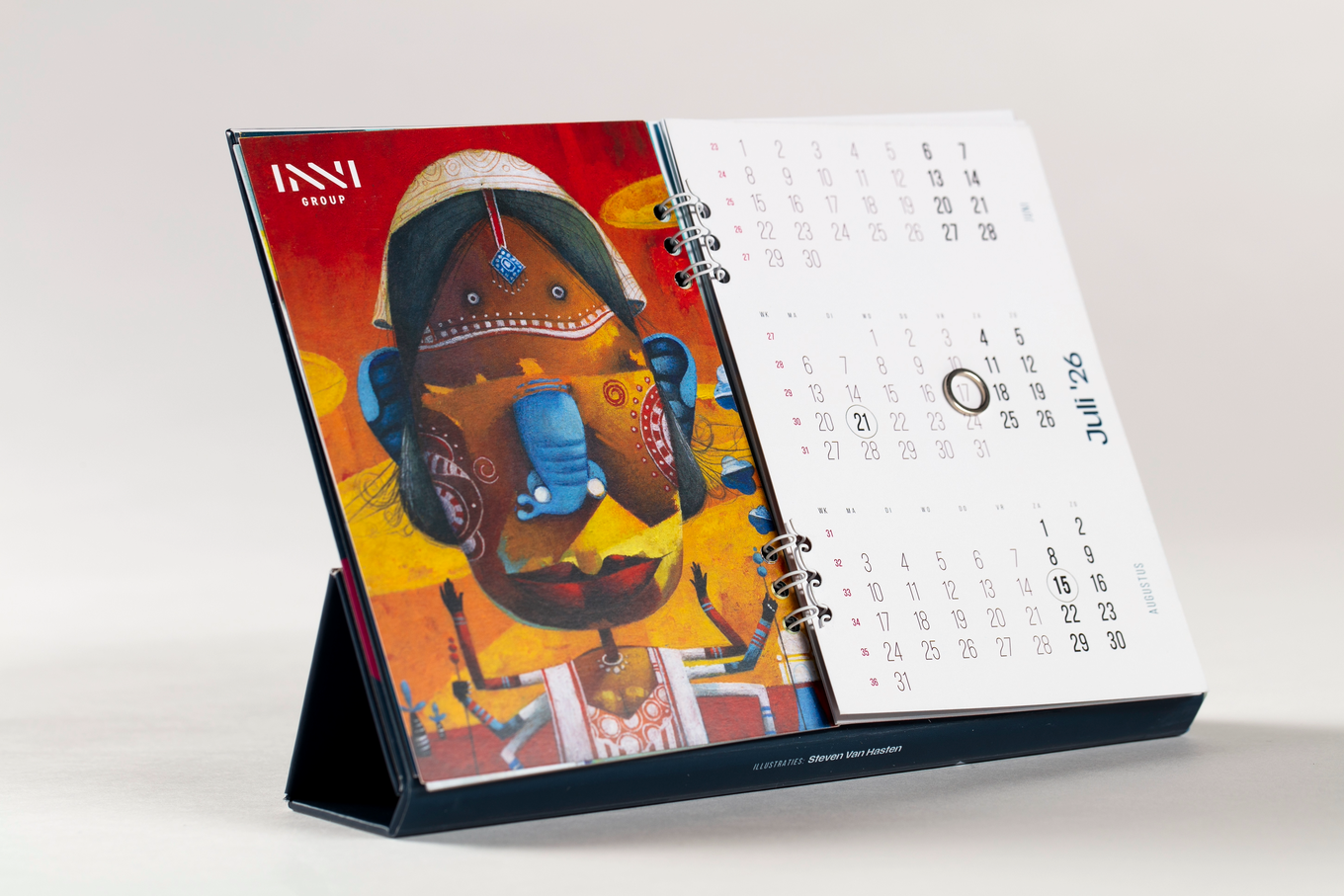 A desk calendar open to July and August, featuring colorful abstract art with a mask-like figure and circular date markers on a stand.