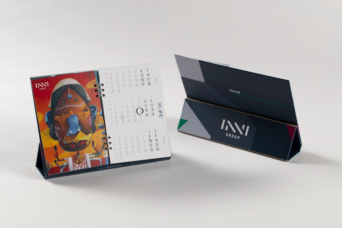 Desk calendar open to July with an artistic image of Ganesh on the left page, placed next to a closed calendar stand with geometric designs.
