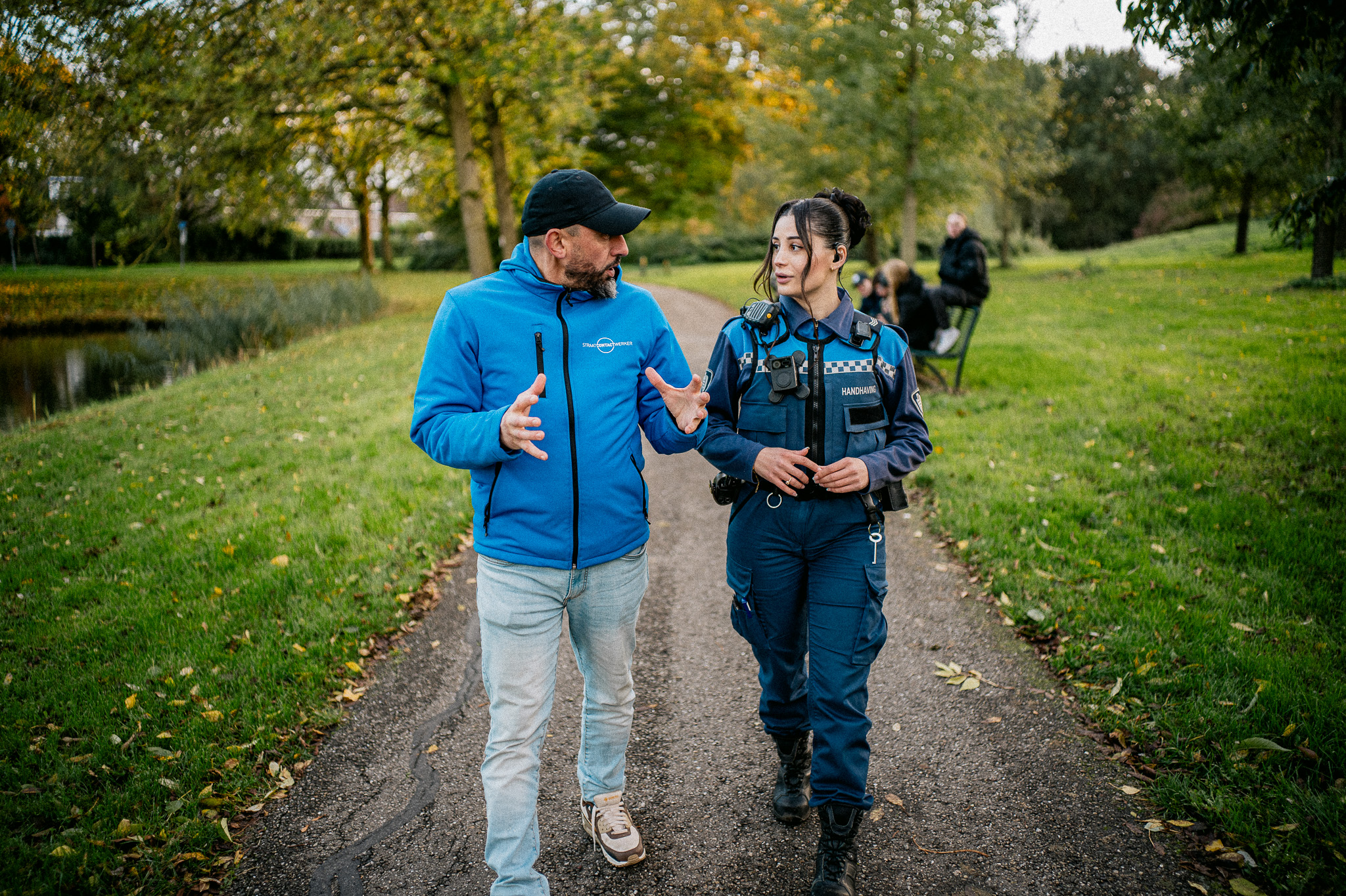 Jongerenwerker in gesprek met Jeugdboa in een parkje met jongeren op de achtergrond