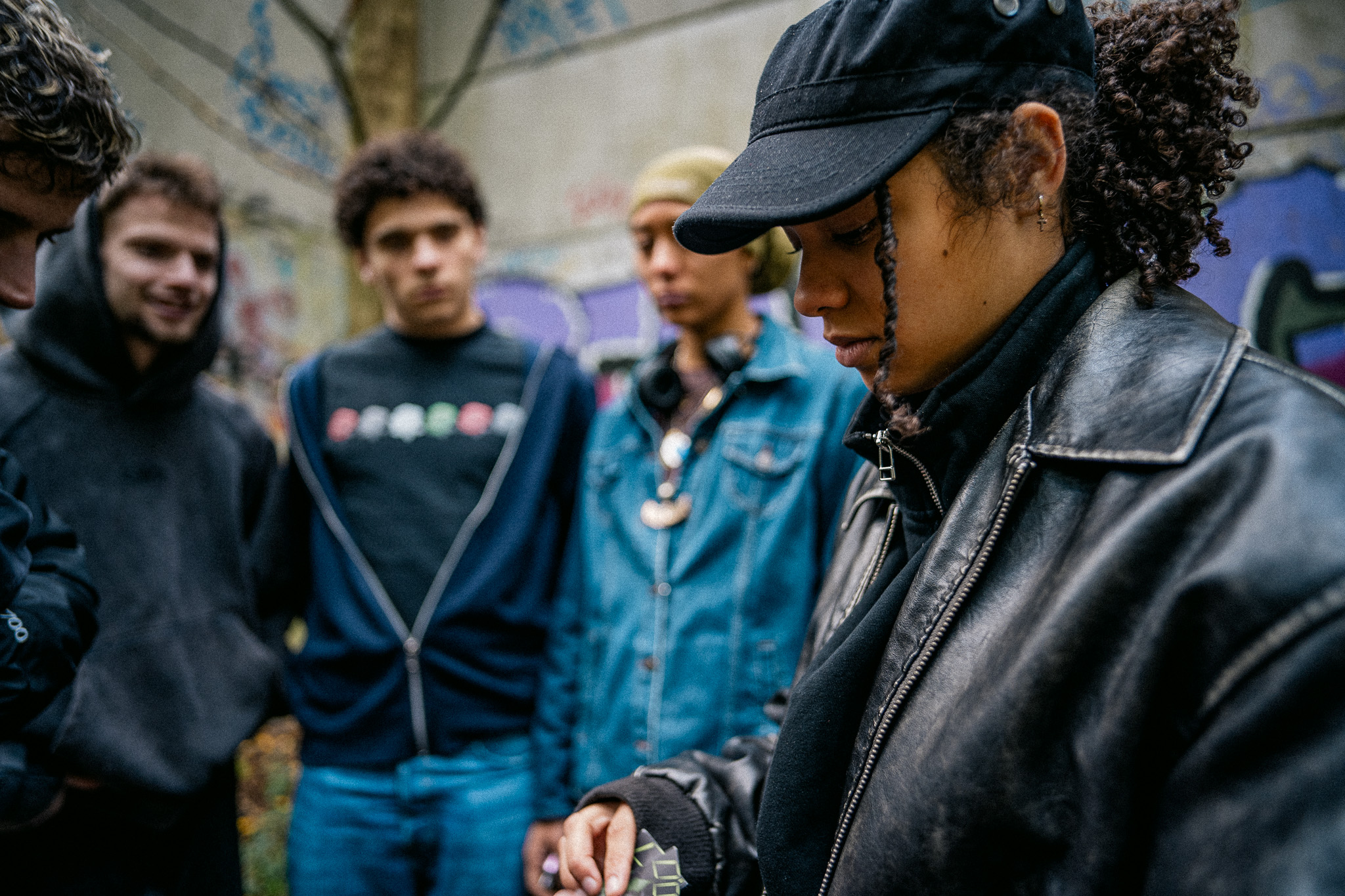 Vrouw aan het dealen op hangplek met jongeren op achtergrond bij graffiti muur