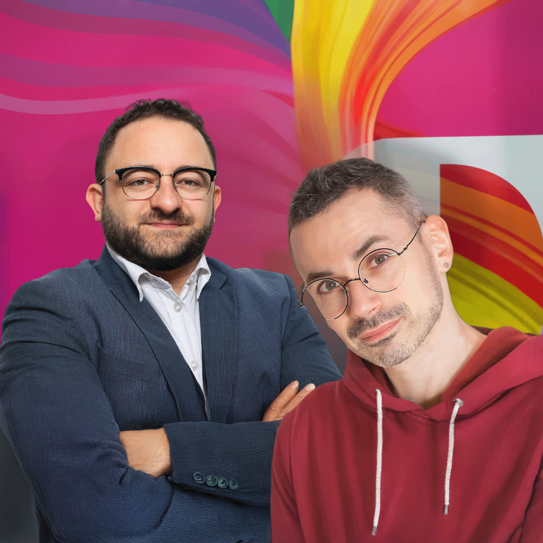 Two men stand in front of a colorful, abstract background. One wears a suit, the other a red hoodie. Both wear glasses and smile slightly.