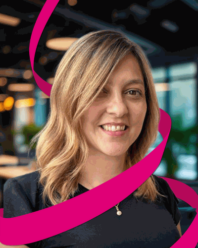 Smiling woman with wavy blonde hair in an office setting, surrounded by a vibrant pink swirl design.