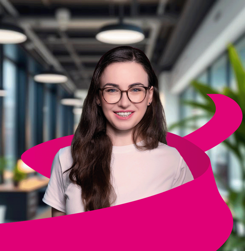 Smiling person with long hair and glasses, wearing a white shirt, with a pink ribbon swirling around, standing in a modern office.