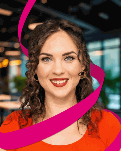 Smiling woman with curly hair and red lipstick, wearing a red top and gold earrings, with a pink ribbon across the image background.