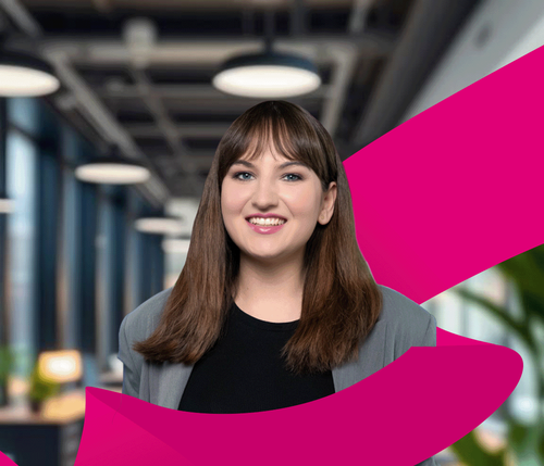 Smiling woman in a gray blazer stands in a modern office with large windows. A pink ribbon graphic swirls around her.