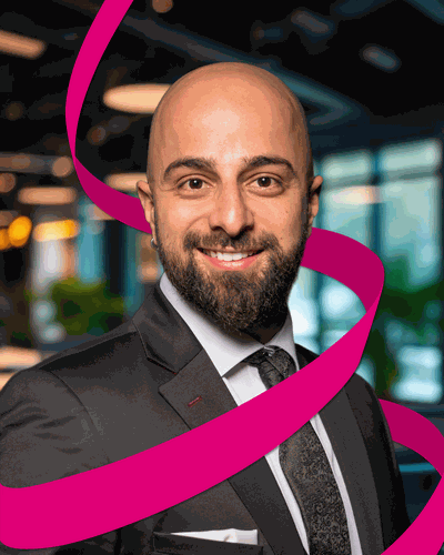 Man in a suit smiling, with a pink ribbon design swirling around him, standing in a modern office setting.