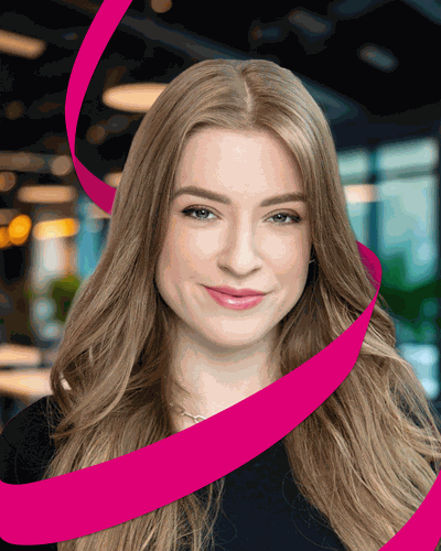 Smiling woman with long hair in a modern office setting, wrapped with a pink ribbon design.