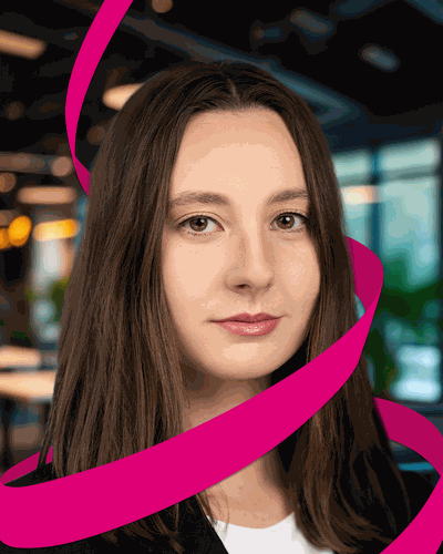 A woman with long brown hair is wrapped in a swirling pink ribbon, set against a blurred indoor background with lights and plants.