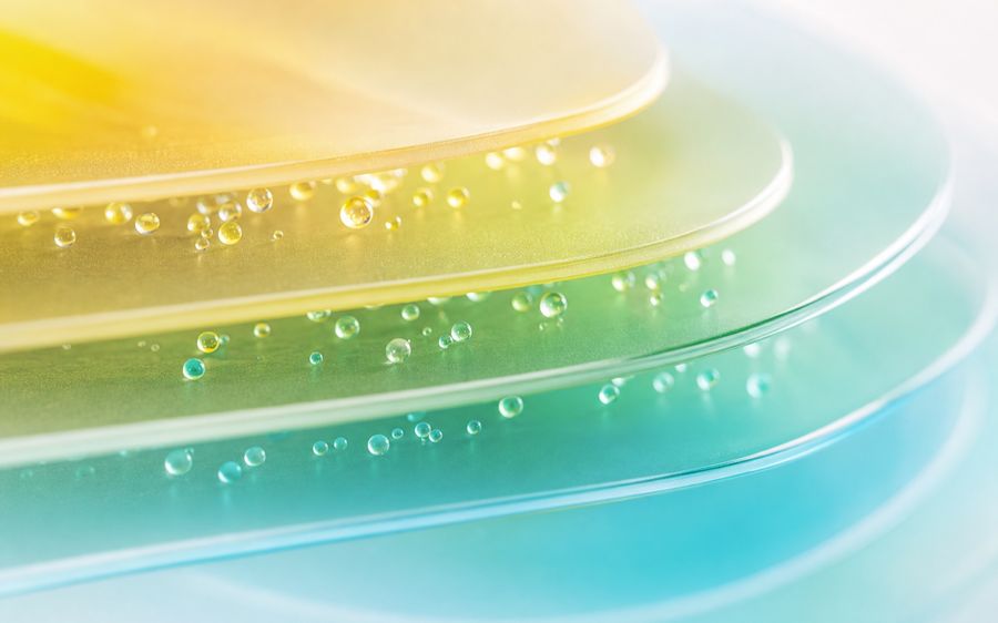 Close-up of colorful layered surfaces with water droplets, transitioning from yellow to green to blue, creating a soothing gradient effect.