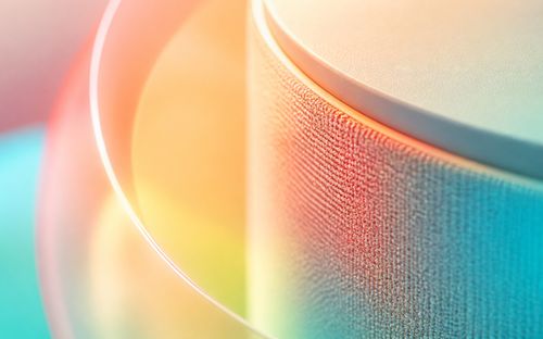 Close-up of two stacked discs with textured surfaces, bathed in vibrant pastel hues of orange, pink, yellow, and teal lighting.